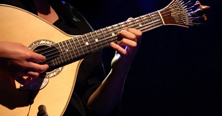 Hände spielen eine birnenförmige zwölfsaitige portugiesische Gitarre auf einer dunklen Bühne