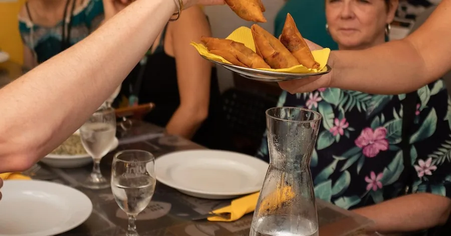 Ein Teller frittierter Kroketten wird über einen Tisch mit Gästen und einem Weinkrug gereicht