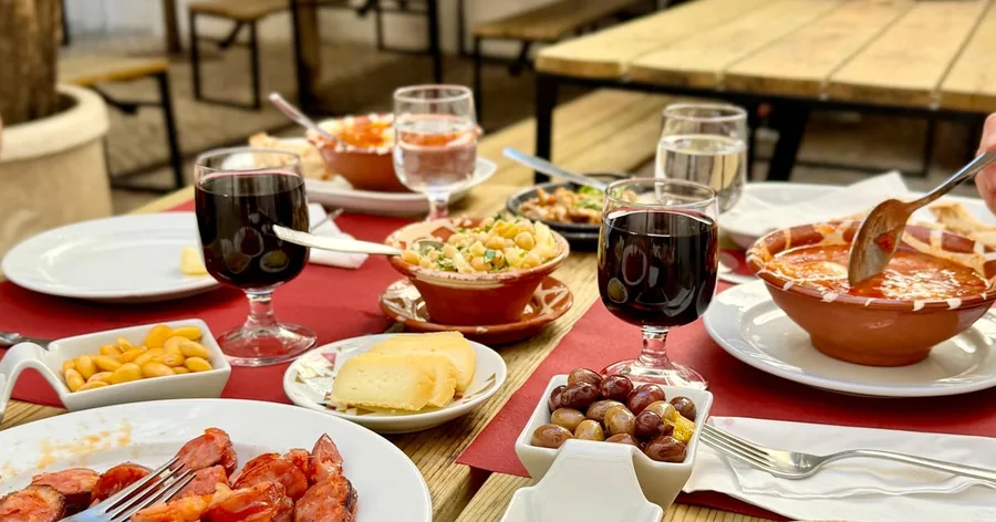 Ein Tavernentisch mit Rotwein, gegrilltem Chouriço, Reis, Käse und kleinen Tellern