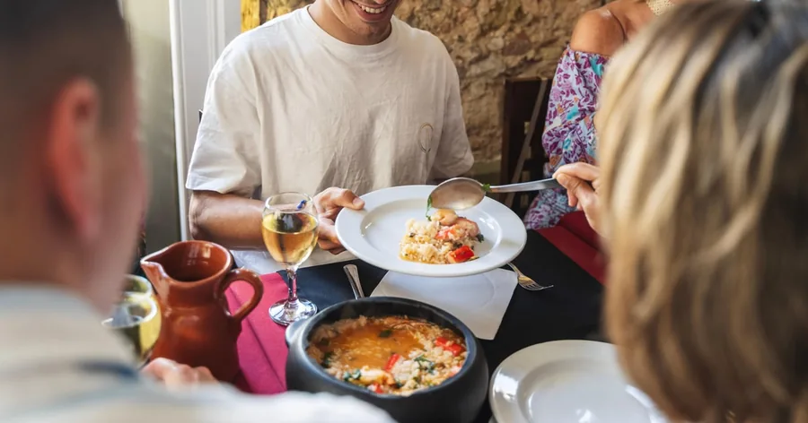 Eine lange Tafel mit Petiscos zum Teilen, Stockfischküchlein, Reis und Weingläsern während eines kulinarischen Rundgangs