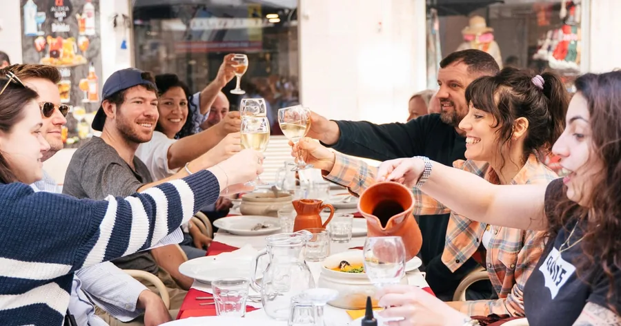 Eine Gruppe hebt an einem belebten Restauranttisch die Weißweingläser über den Tellern